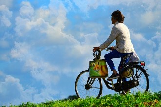 Mulher andando de bicicleta com céu azul ao fundo